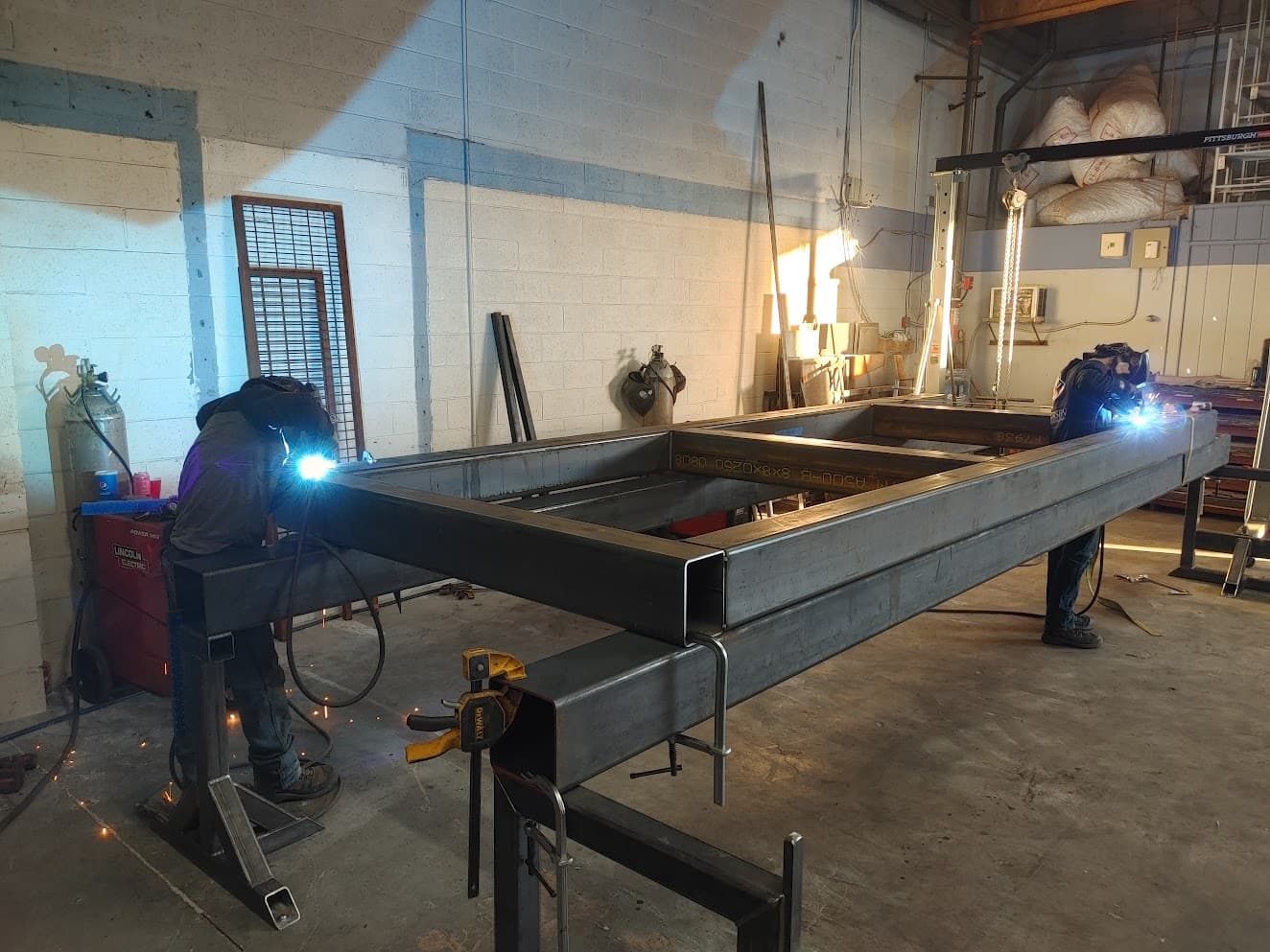 Two employees work together welding a structural piece